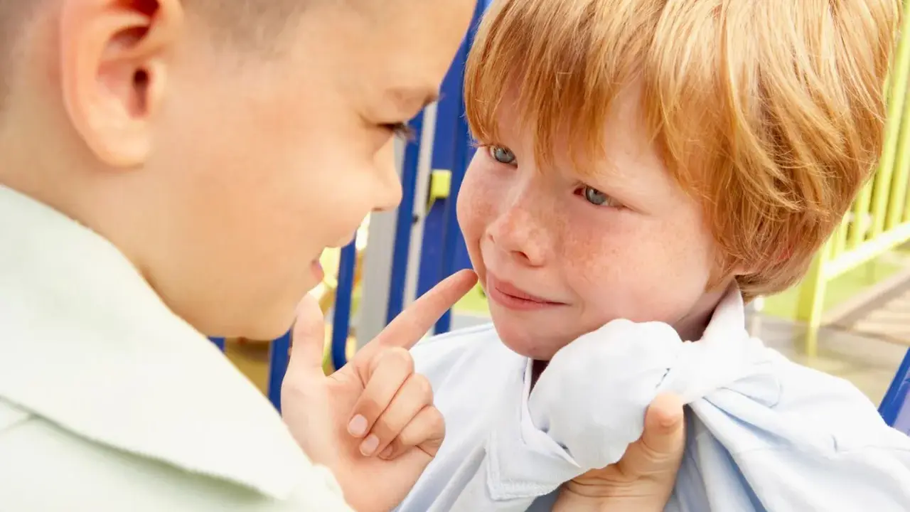 Ein Junge zeigt mit dem Finger auf das Gesicht eines anderen Jungen, der verängstigt wirkt. Ein Beispiel für Mobbing in der Schule.