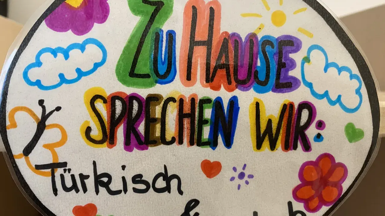 Bunte Zeichnung mit der Aufschrift "Zu Hause sprechen wir: Türkisch & Deutsch". Ein Beispiel für vorurteilsbewusste Pädagogik, die Mehrsprachigkeit feiert.