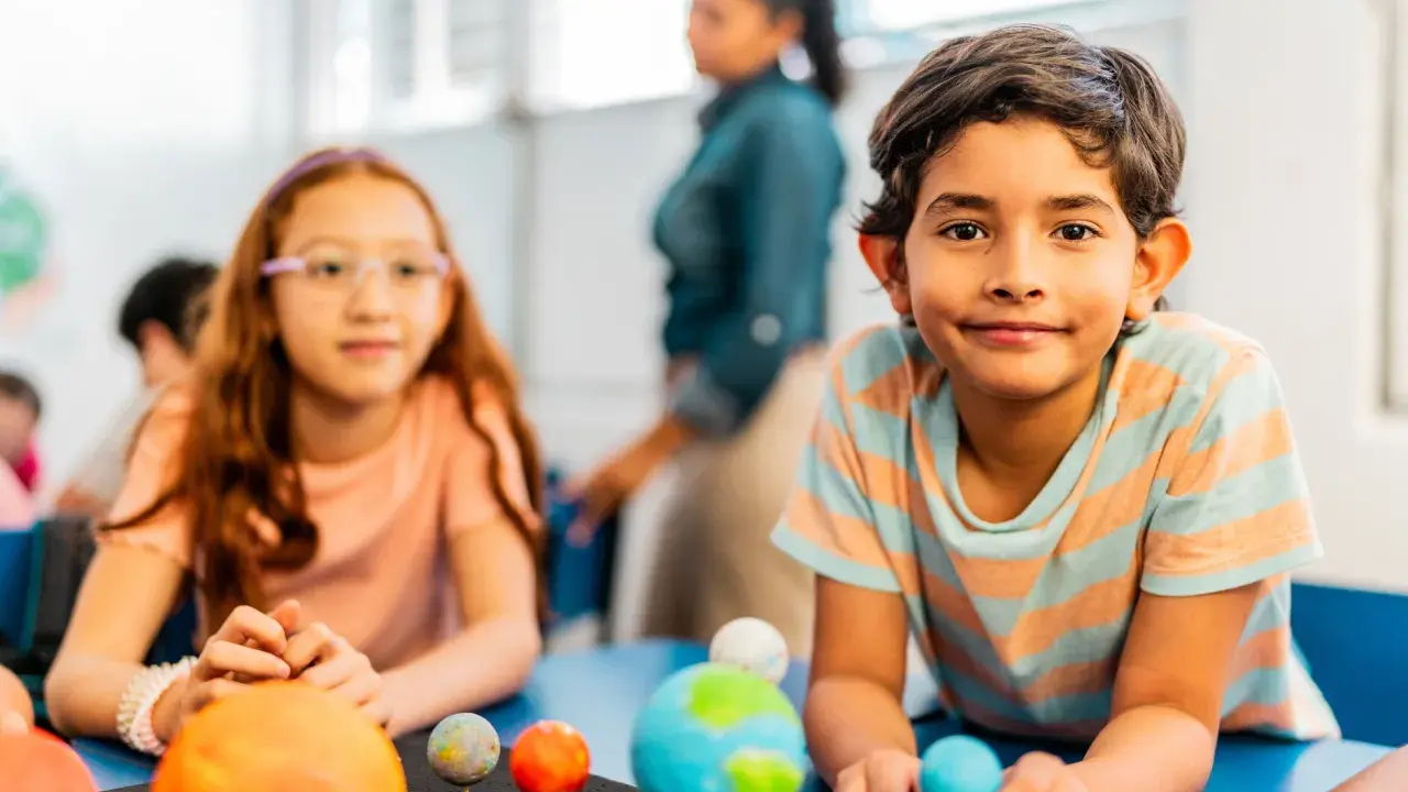 Kinder lernen spielerisch über das Sonnensystem. Ein Junge hält eine Himmelskugel, während ein Mädchen mit einem Modell des Sonnensystems experimentiert. Dies sind Beispiele für alternative Schulkonzepte.