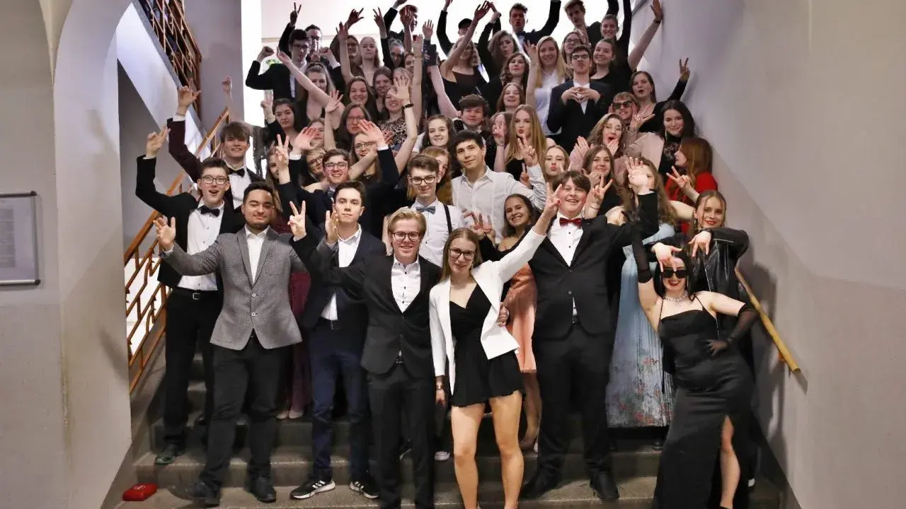 Schüler feiern Mottowoche Filme und Serien auf einer Treppe, alle in schicken Outfits, viele mit V-Gesten.