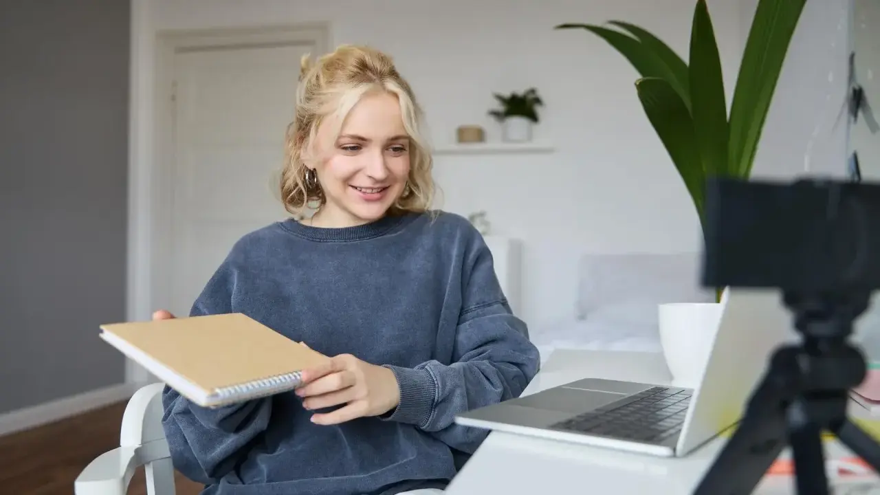 Junge Frau gibt online Nachhilfe, hält ein Notizbuch und lächelt in die Kamera.