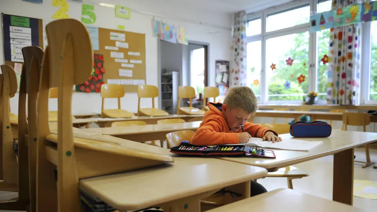 Ein Junge lernt allein im Klassenzimmer. Die leeren Stühle erinnern an eine kollektivstrafe, die er nicht verdient hat.