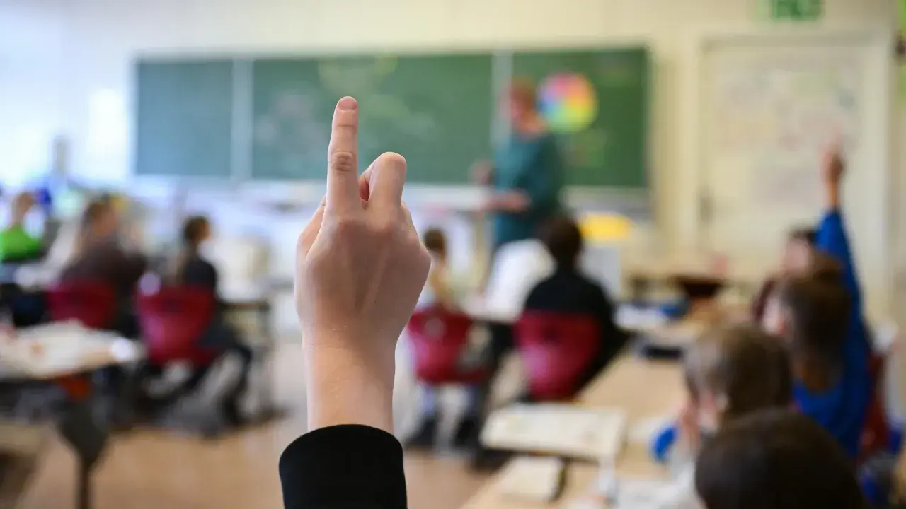 Ein Finger zeigt nach oben im Klassenzimmer. Dies symbolisiert die **Schulpflicht in Deutschland**, wo Kinder lernen und Fragen stellen.