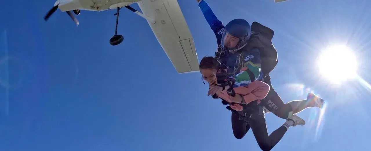 Ein Tandem-Fallschirmsprung – die perfekte Antwort auf die Frage, was schenkt man zum bestandenen Abitur. Zwei Menschen genießen den freien Fall vor strahlend blauem Himmel.