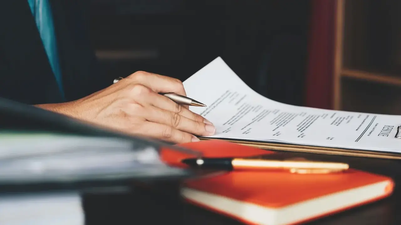 Person überarbeitet ein Resume, um einen Artikel auf Englisch zu schreiben. Ein Stift liegt auf einem Notizbuch.