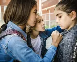 Drei Mädchen stehen eng beieinander. Ein Mädchen wirkt bedrängt, was auf Mobbing in der Grundschule hindeutet.