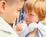Ein Junge zeigt mit dem Finger auf das Gesicht eines anderen Jungen, der verängstigt wirkt. Ein Beispiel für Mobbing in der Schule.