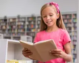 Ein Mädchen mit pinkem Haarband liest in der Schulbibliothek. Ein Beispiel für Leseförderung in der Grundschule, das Freude am Buch zeigt.
