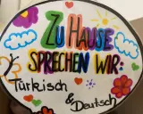 Bunte Zeichnung mit der Aufschrift "Zu Hause sprechen wir: Türkisch & Deutsch". Ein Beispiel für vorurteilsbewusste Pädagogik, die Mehrsprachigkeit feiert.