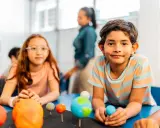 Kinder lernen spielerisch über das Sonnensystem. Ein Junge hält eine Himmelskugel, während ein Mädchen mit einem Modell des Sonnensystems experimentiert. Dies sind Beispiele für alternative Schulkonzepte.