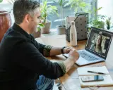 Mann gibt online Nachhilfe. Er lächelt und spricht mit einer Frau auf seinem Laptop.
