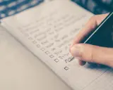 Hand schreibt eine Liste mit Aufgaben auf Englisch. Die Liste enthält Punkte wie "Drive" und "Move", die an eine Aufzählung von Stilmitteln erinnern.