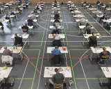 Viele Schüler sitzen in einer Sporthalle an Tischen, um zum Abitur zu schreiben.