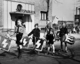 Jungen in Uniformen marschieren mit Fahnen und Trommel vor der Stadtsparkasse. Ein Bild der vermeintlichen Volksgemeinschaft.