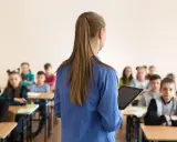Lehrerin mit Tablet vor Schülern. Die Frage "wie viel verdient ein lehrer" beschäftigt viele.
