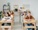 Schüler sitzen an Holztischen in einem hellen Klassenzimmer. Eine mögliche Sitzordnung für unruhige Klassen, die Konzentration fördert.