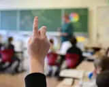 Ein Finger zeigt nach oben im Klassenzimmer. Dies symbolisiert die **Schulpflicht in Deutschland**, wo Kinder lernen und Fragen stellen.
