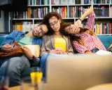 Drei erschöpfte Studenten schlafen auf einer Couch, umgeben von Büchern. Der abi deutsch-Test war wohl zu anstrengend.