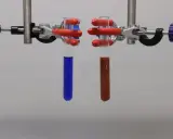 Zwei Reagenzgläser mit Flüssigkeiten, eines blau, das andere rotbraun, werden in einem Laborständer für eine Fehling-Probe gehalten.