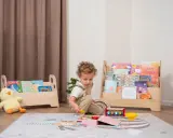 Kleines Kind spielt mit Holzspielzeug vor einem Regal mit Büchern, das eine Sitzordnung im Montessori-Stil widerspiegelt.