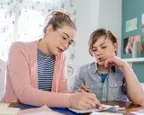 Junge Frau bietet Nachhilfe an. Sie erklärt einem Jungen konzentriert eine Aufgabe auf Papier.