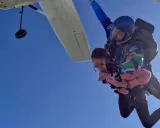 Ein Tandem-Fallschirmsprung – die perfekte Antwort auf die Frage, was schenkt man zum bestandenen Abitur. Zwei Menschen genießen den freien Fall vor strahlend blauem Himmel.