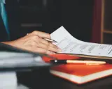 Person überarbeitet ein Resume, um einen Artikel auf Englisch zu schreiben. Ein Stift liegt auf einem Notizbuch.