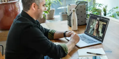 Mann gibt online Nachhilfe. Er lächelt und spricht mit einer Frau auf seinem Laptop.