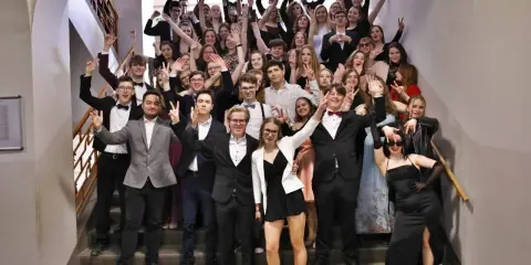 Schüler feiern Mottowoche Filme und Serien auf einer Treppe, alle in schicken Outfits, viele mit V-Gesten.