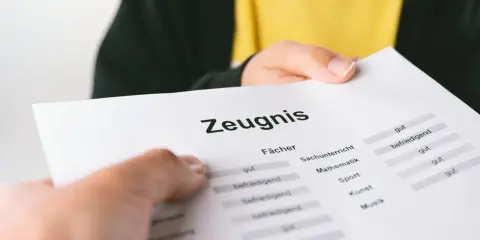 Ein Zeugnis wird überreicht. Die Noten sind gemischt, von "gut" bis "befriedigend", aber keine "ungenügend" Note.