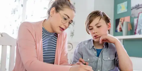 Junge Frau bietet Nachhilfe an. Sie erklärt einem Jungen konzentriert eine Aufgabe auf Papier.