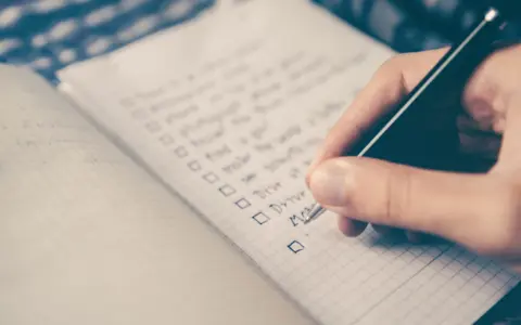 Hand schreibt eine Liste mit Aufgaben auf Englisch. Die Liste enthält Punkte wie "Drive" und "Move", die an eine Aufzählung von Stilmitteln erinnern.