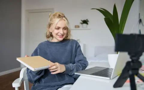 Junge Frau gibt online Nachhilfe, hält ein Notizbuch und lächelt in die Kamera.
