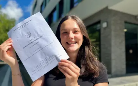 Stolze Schülerin mit Abiturzeugnis in der Hand. Sie fragt sich, wie viele Punkte für 0,9 Abi nötig sind.