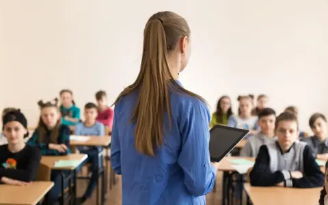 Lehrerin mit Tablet vor Schülern. Die Frage "wie viel verdient ein lehrer" beschäftigt viele.