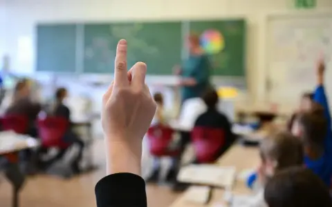 Ein Finger zeigt nach oben im Klassenzimmer. Dies symbolisiert die **Schulpflicht in Deutschland**, wo Kinder lernen und Fragen stellen.