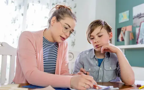 Junge Frau bietet Nachhilfe an. Sie erklärt einem Jungen konzentriert eine Aufgabe auf Papier.