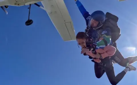 Ein Tandem-Fallschirmsprung – die perfekte Antwort auf die Frage, was schenkt man zum bestandenen Abitur. Zwei Menschen genießen den freien Fall vor strahlend blauem Himmel.