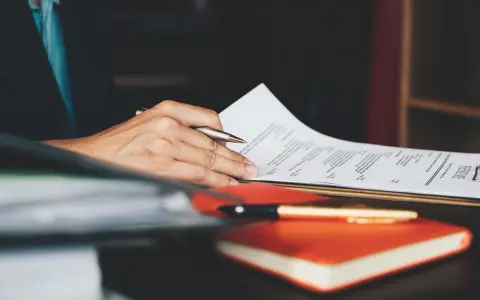 Person überarbeitet ein Resume, um einen Artikel auf Englisch zu schreiben. Ein Stift liegt auf einem Notizbuch.