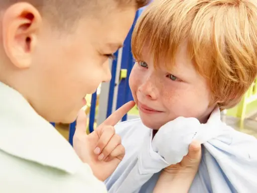 Ein Junge zeigt mit dem Finger auf das Gesicht eines anderen Jungen, der verängstigt wirkt. Ein Beispiel für Mobbing in der Schule.