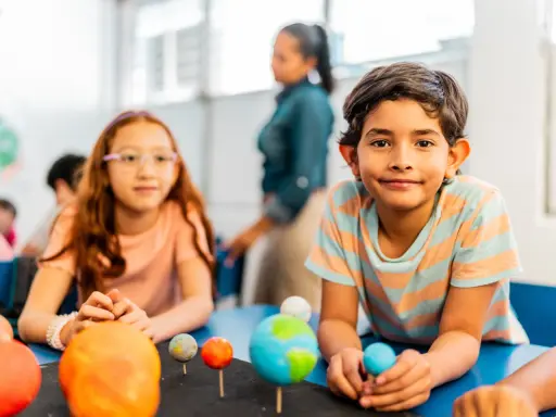 Kinder lernen spielerisch über das Sonnensystem. Ein Junge hält eine Himmelskugel, während ein Mädchen mit einem Modell des Sonnensystems experimentiert. Dies sind Beispiele für alternative Schulkonzepte.