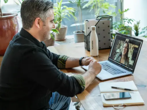 Mann gibt online Nachhilfe. Er lächelt und spricht mit einer Frau auf seinem Laptop.