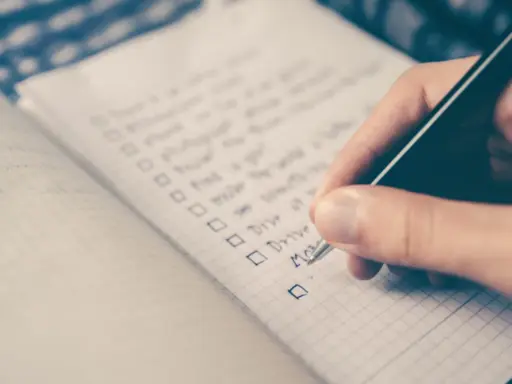 Hand schreibt eine Liste mit Aufgaben auf Englisch. Die Liste enthält Punkte wie "Drive" und "Move", die an eine Aufzählung von Stilmitteln erinnern.