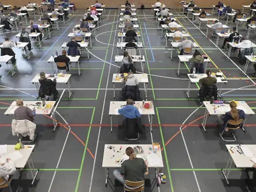 Viele Schüler sitzen in einer Sporthalle an Tischen, um zum Abitur zu schreiben.