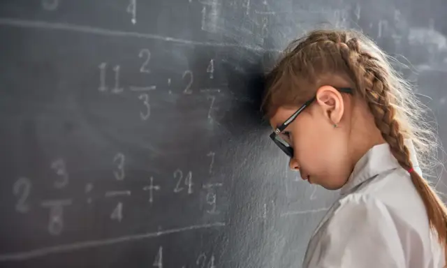 Mädchen mit Brille lehnt frustriert am Tafelbild mit Matheaufgaben. Die note 5 in der schule ist zu viel.