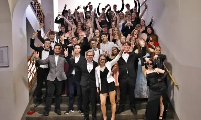 Schüler feiern Mottowoche Filme und Serien auf einer Treppe, alle in schicken Outfits, viele mit V-Gesten.