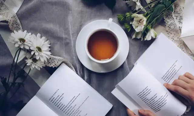 Eine Tasse Tee, Blumen und ein Buch mit einem wehmütigen Gedicht.