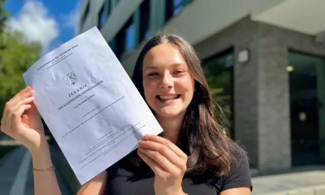 Stolze Schülerin mit Abiturzeugnis in der Hand. Sie fragt sich, wie viele Punkte für 0,9 Abi nötig sind.