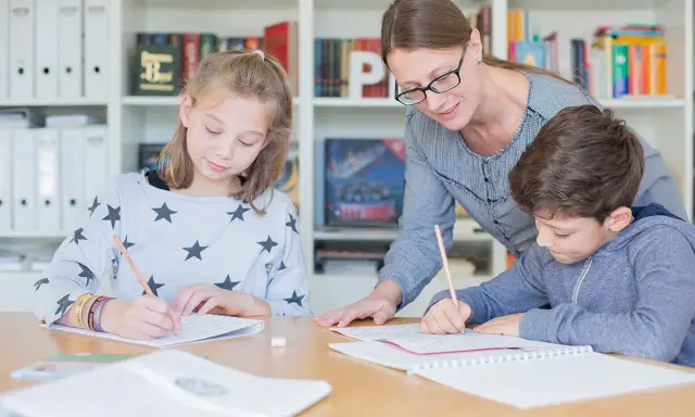 Lehrerin hilft zwei Schülern bei der Nachhilfe Realschule. Sie schreiben konzentriert in ihre Hefte.