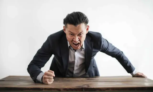 Wütender Mann im Anzug schreit über einen Tisch. Darf ein Lehrer Schüler anschreien?